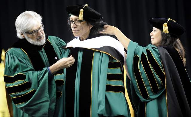 Paul Massaron and Sandra Hughes O'Brien, members of the Wayne State University Board of Governors, put the sash on Sixto Rodriguez during commencement ceremonies at Ford Field. (David Coates/The Detroit News)